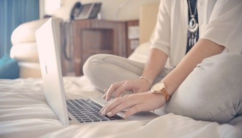 Chica escribiendo en un ordenador en la cama